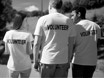 Three people wearing t-shirts that display the word VOLUNTEER on their backs